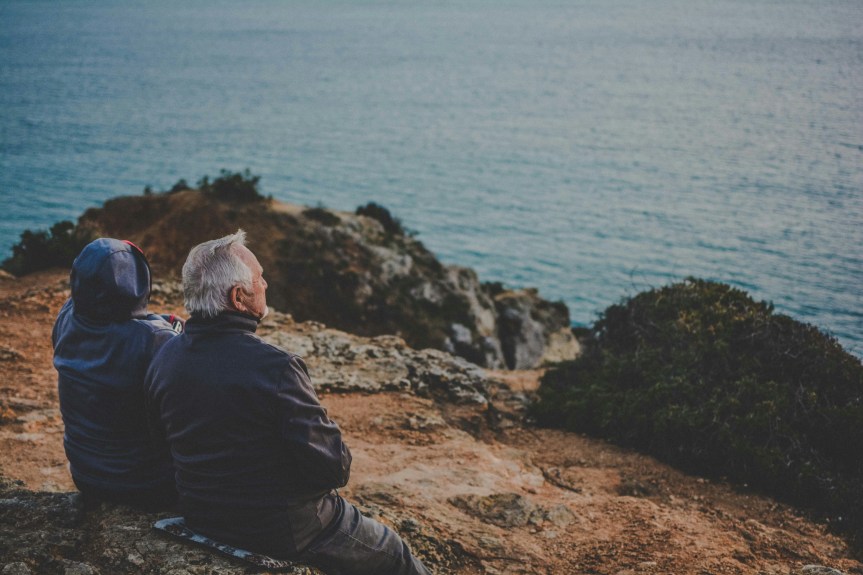 Photo of someone sitting by the ocean with and aging person.