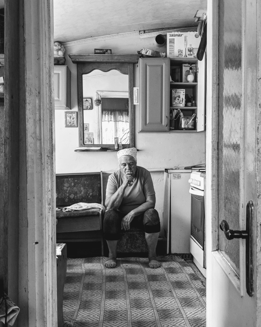 Photo of elderly person sitting in her kitchen with her hand covering her mouth.